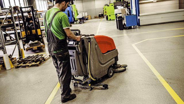 Janitor cleaning industrial floor with machine
